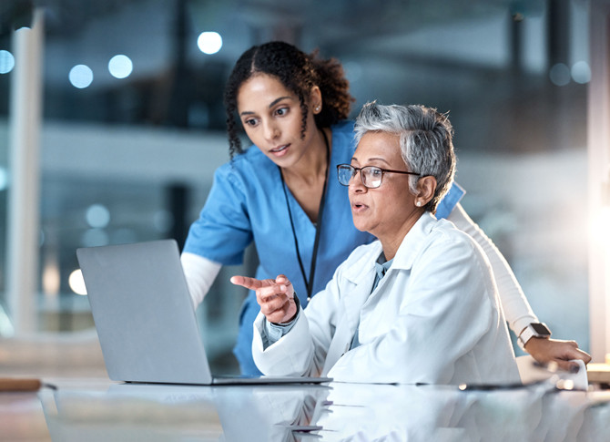 A nurse and a doctor engaged in a discussion while examining information on a laptop.