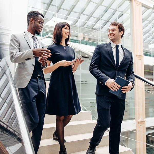 Three happy multiracial business people walking down on stairs together with digital tablet