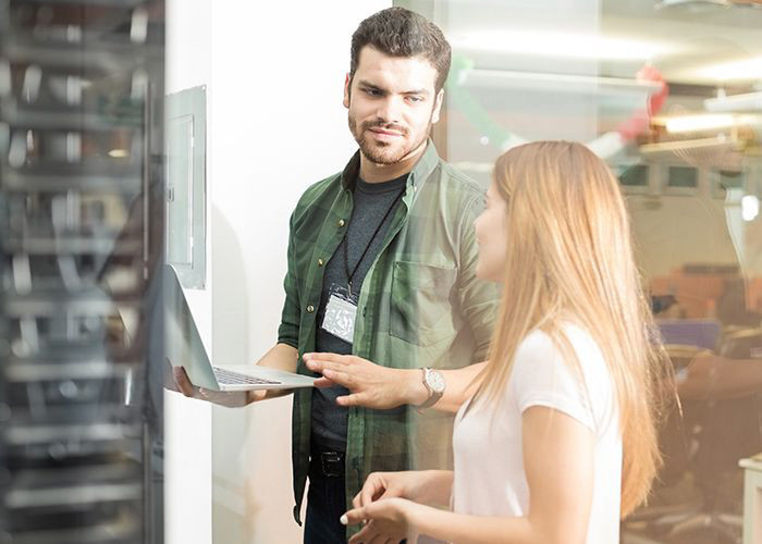 Two business people standing in server room with laptop and discussing