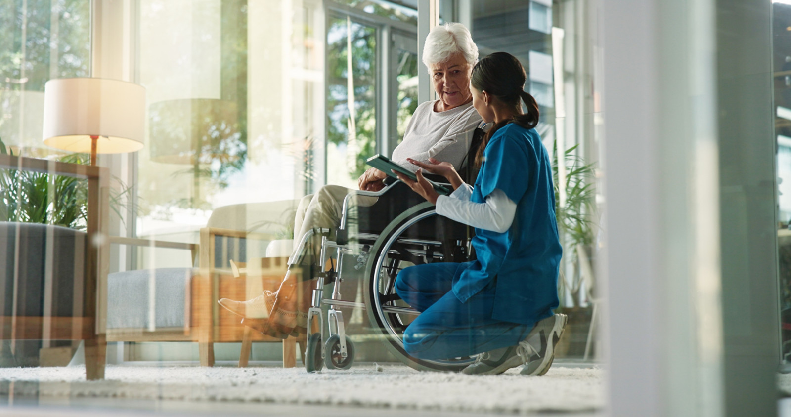 Women, nurse and mature patient in wheelchair at retirement home for healthcare, support and checkup. Caregiver, person with disability and tablet for medical service, physiotherapy and discussion.