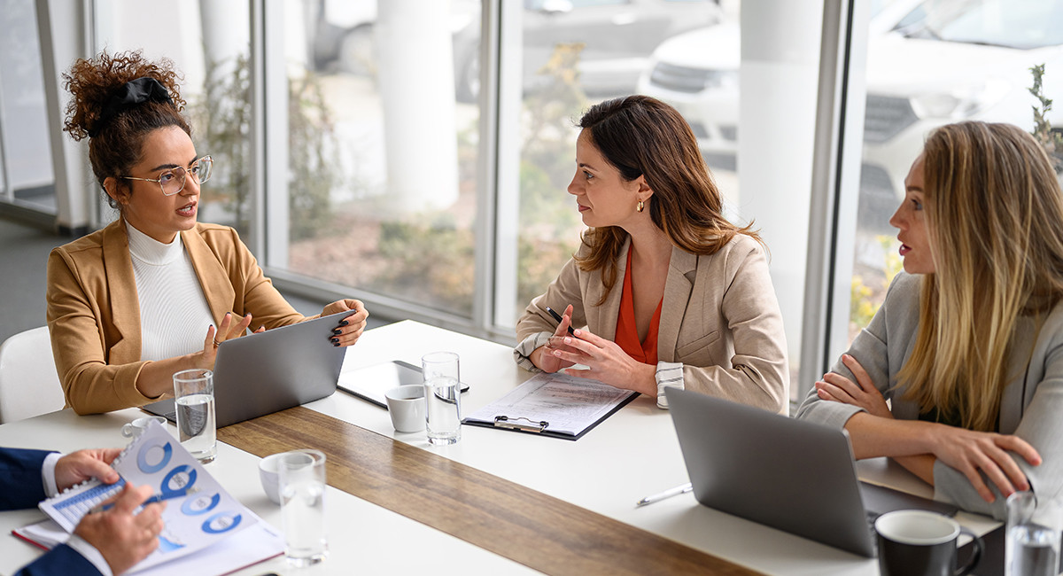 A group of four professionals in an office, intently discussing a complex digital diagram on a large screen.