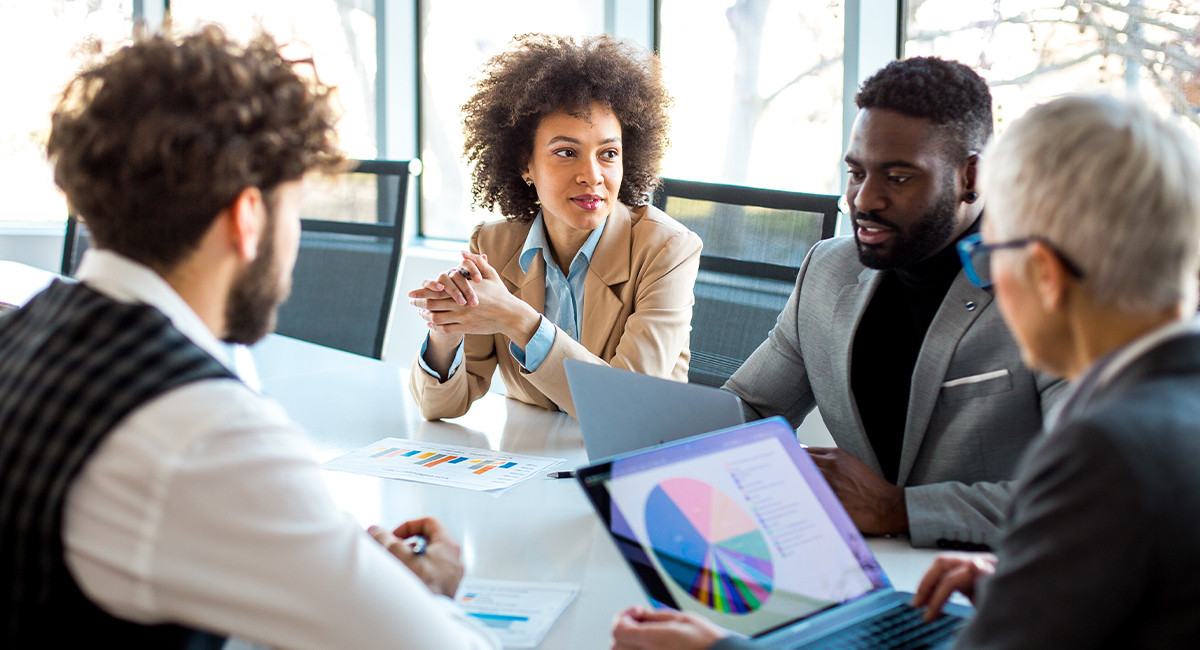 A diverse group of people gathered around a table, collaborating with a laptop in the center.