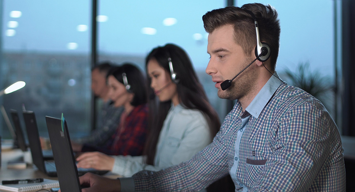 men and women sitting in front of a laptop with headset