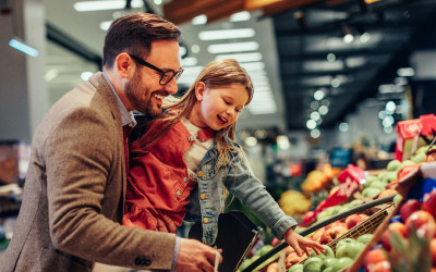 A father carryhing his daughter purchasing frutis in a retail store