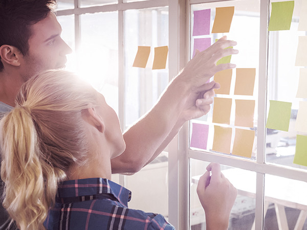 A man and woman examine colorful sticky notes arranged on a wall