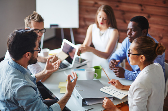 A group of diverse individuals seated around a table, each using a laptop for collaborative work.