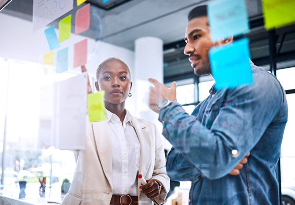 A man and woman looking at board with sticky notes