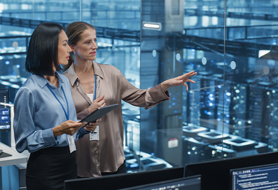 Two women in business attire collaborating while looking at a computer screen in a professional setting.