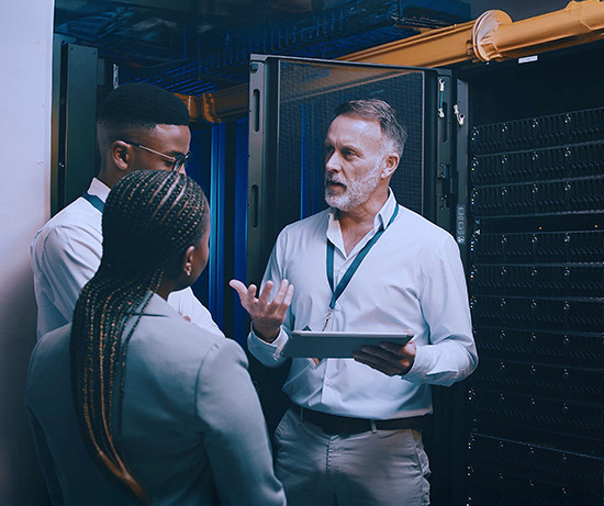 A group of three professionals in a server room discuss work