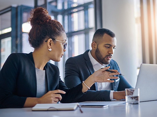 A man and woman stand beside a whiteboard, engaged in discussion