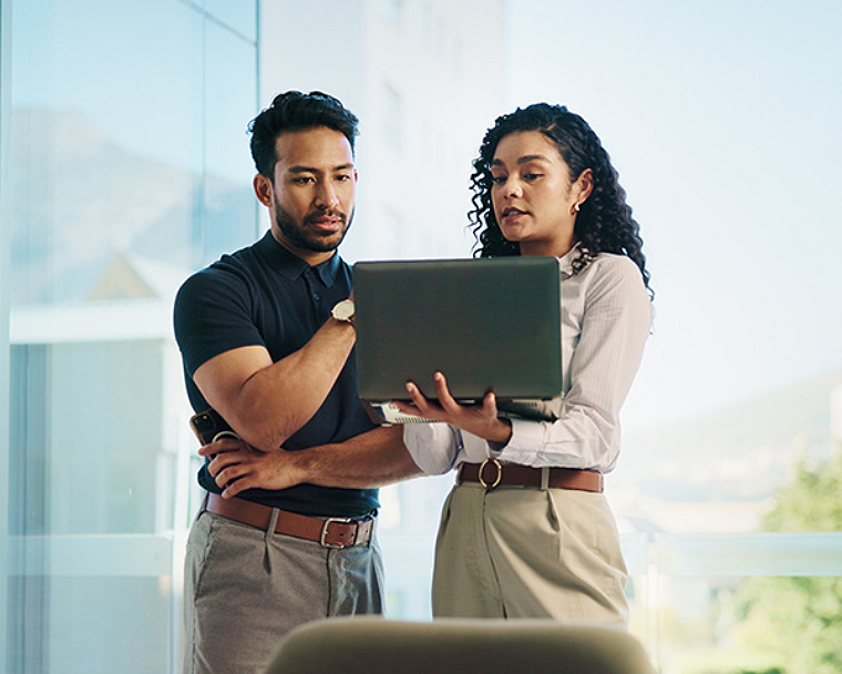 A man and woman standing and discussing with laptop.