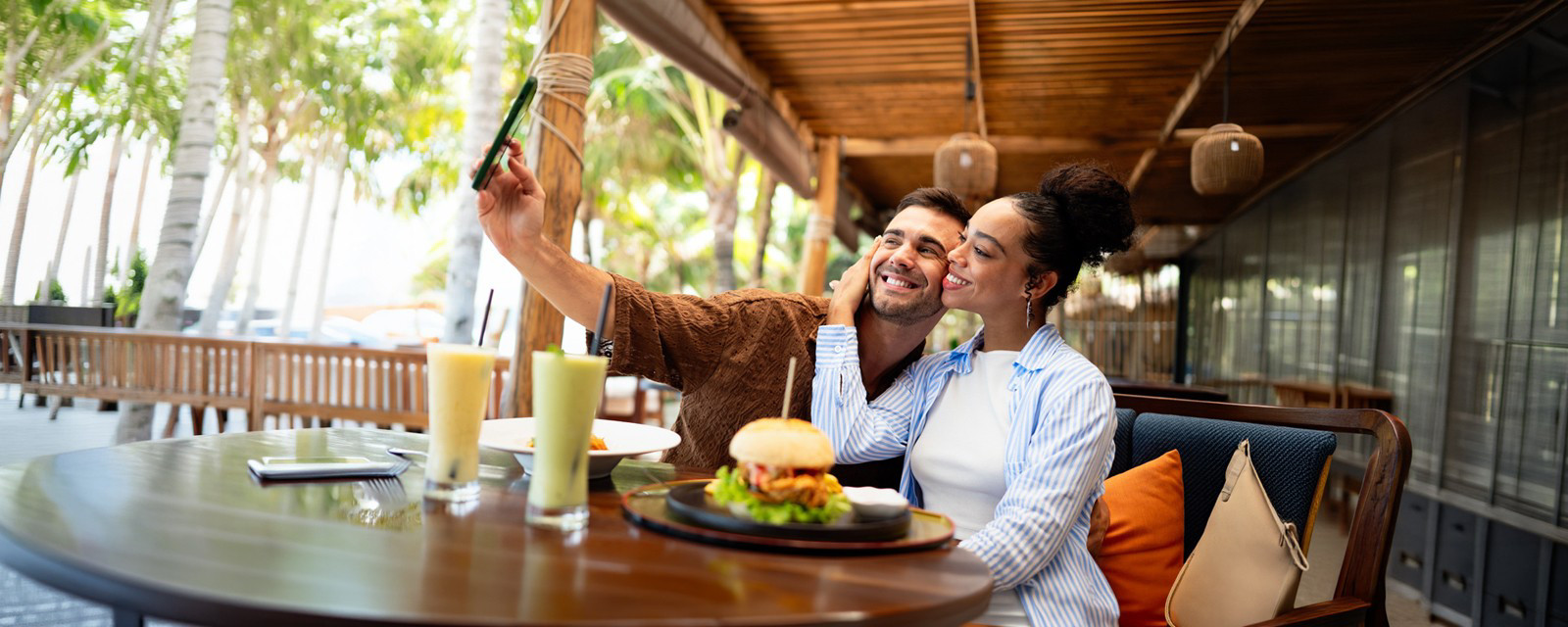 A man and woman happily taking a selfie together, with their appetizing food spread visible in the foreground.