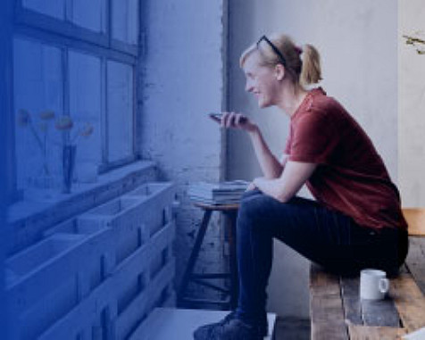 lady sitting on a bench next to a window holding a mobile phone