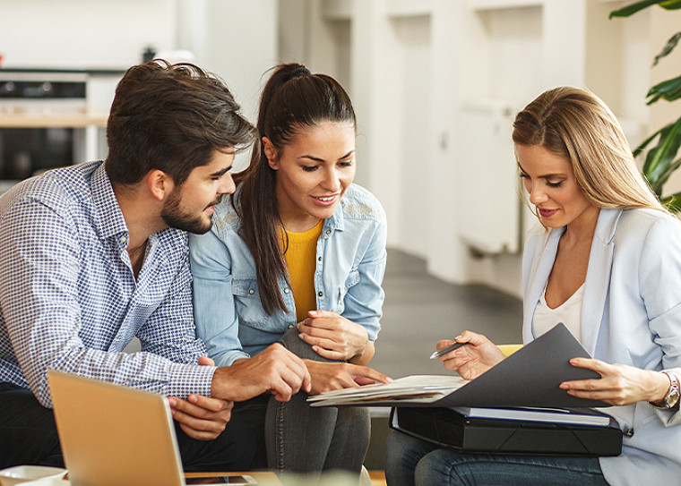 A professional sitting at a table and showing a document file to two customers