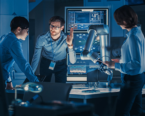 Three people standing over a desk with high-tech monitors and robotics