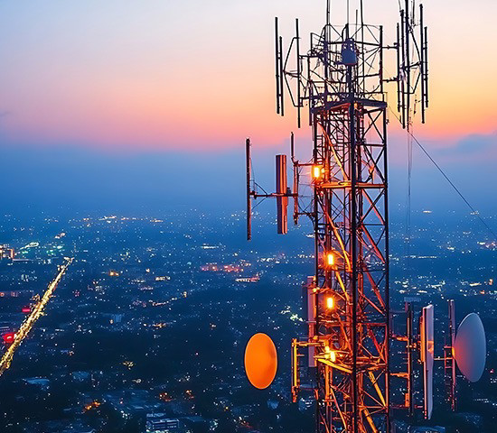 Le soleil couchant entoure les antennes de téléphonie mobile d'un liseré chaleureux avec la ville en toile de fond, soulignant ainsi l'importance de la connectivité des télécommunications.
