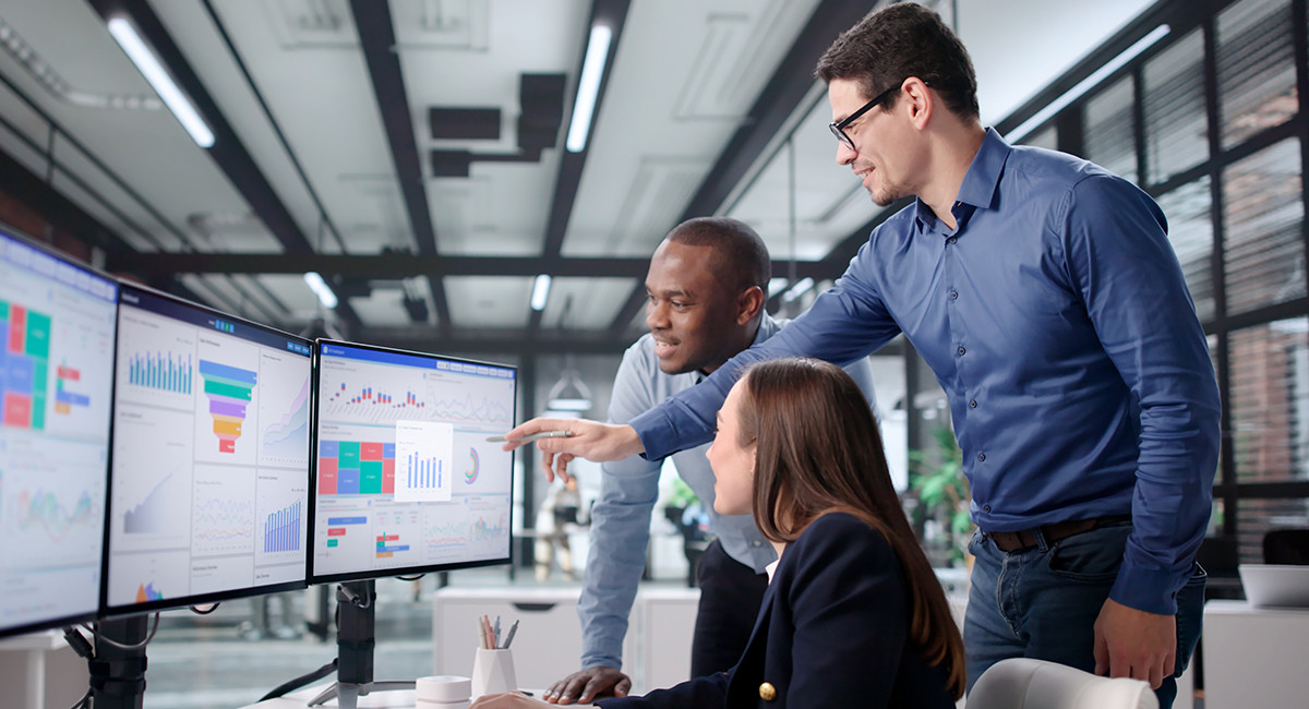 A group of four professionals in an office, intently discussing a complex digital diagram on a large screen.