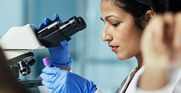 mujer mirando a través de un microscopio