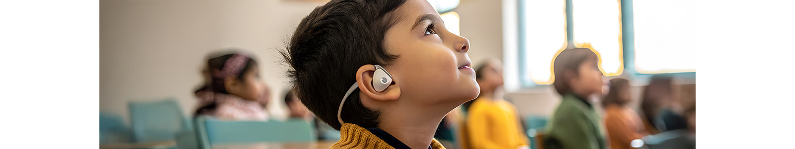 In a classroom, a child with headphones is engaged in learning at their desk.