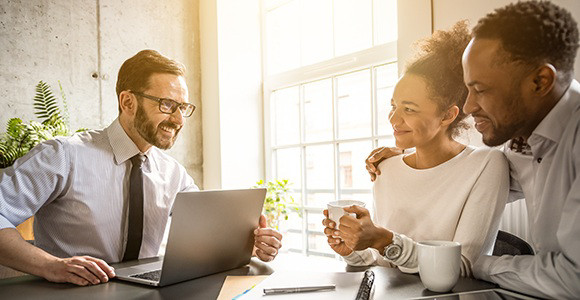 An male agent with a laptop open is consulting a couple who are sitting across a table
