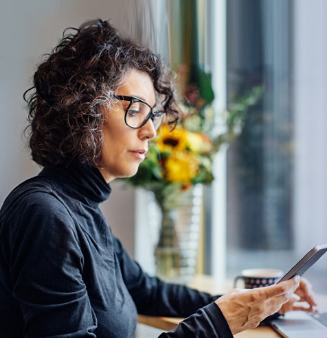 Frau schaut auf ihr Handy und arbeitet an ihrem Laptop