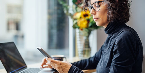 Frau schaut auf ihr Handy und arbeitet an ihrem Laptop