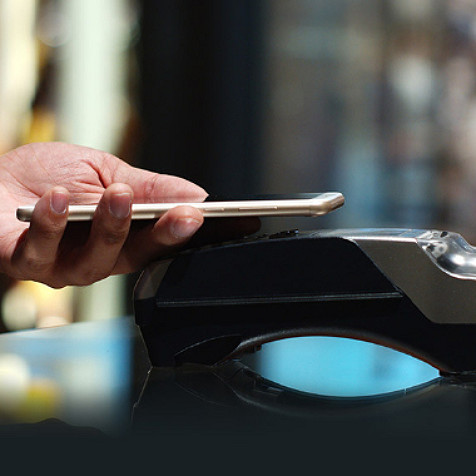 Personne tenant son téléphone portable à la main pour le scanner sur le lecteur de carte de paiement et effectuer un paiement