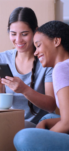 Zwei Frauen im Schneidersitz lächeln und schauen auf ein Mobiltelefon