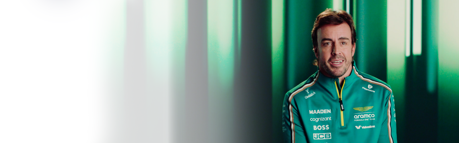 An F1 car racer in a green racing suit smiles broadly.