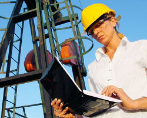 femme portant un casque devant une installation pétrolière