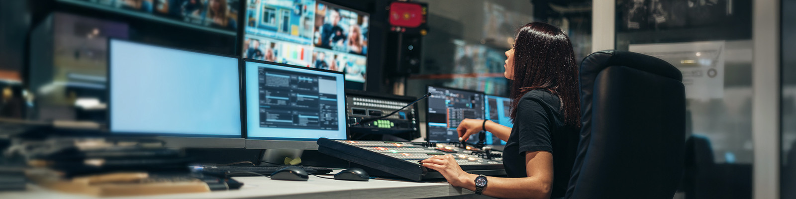 A woman sits at a desk, focused on multiple computer monitors displaying various applications and data.