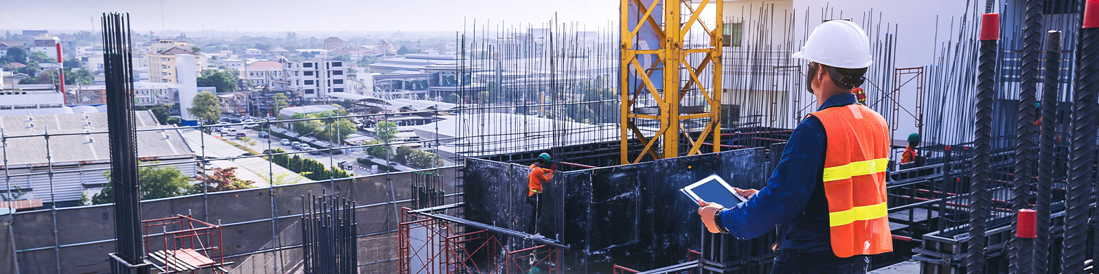 A construction worker wearing a hard hat and safety vest, actively working on a construction site with machinery in the background.