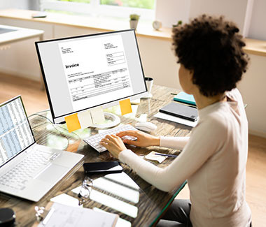 A woman working at a computer and a laptop