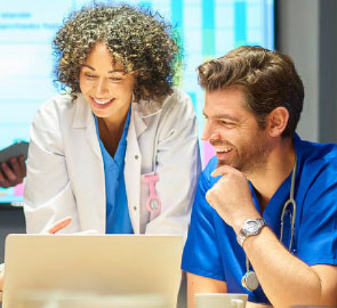 Two medical professionals smiling and looking at a laptop