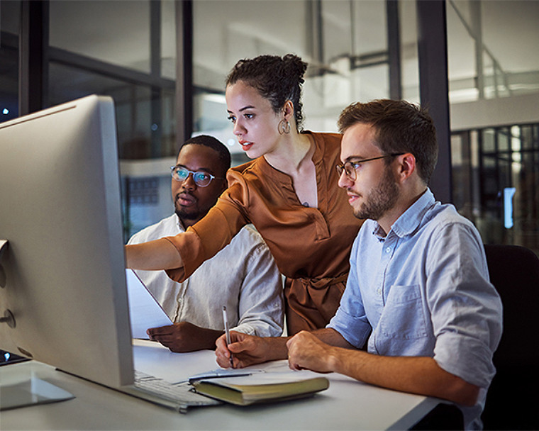 Three professionals working on desktop computers in an office