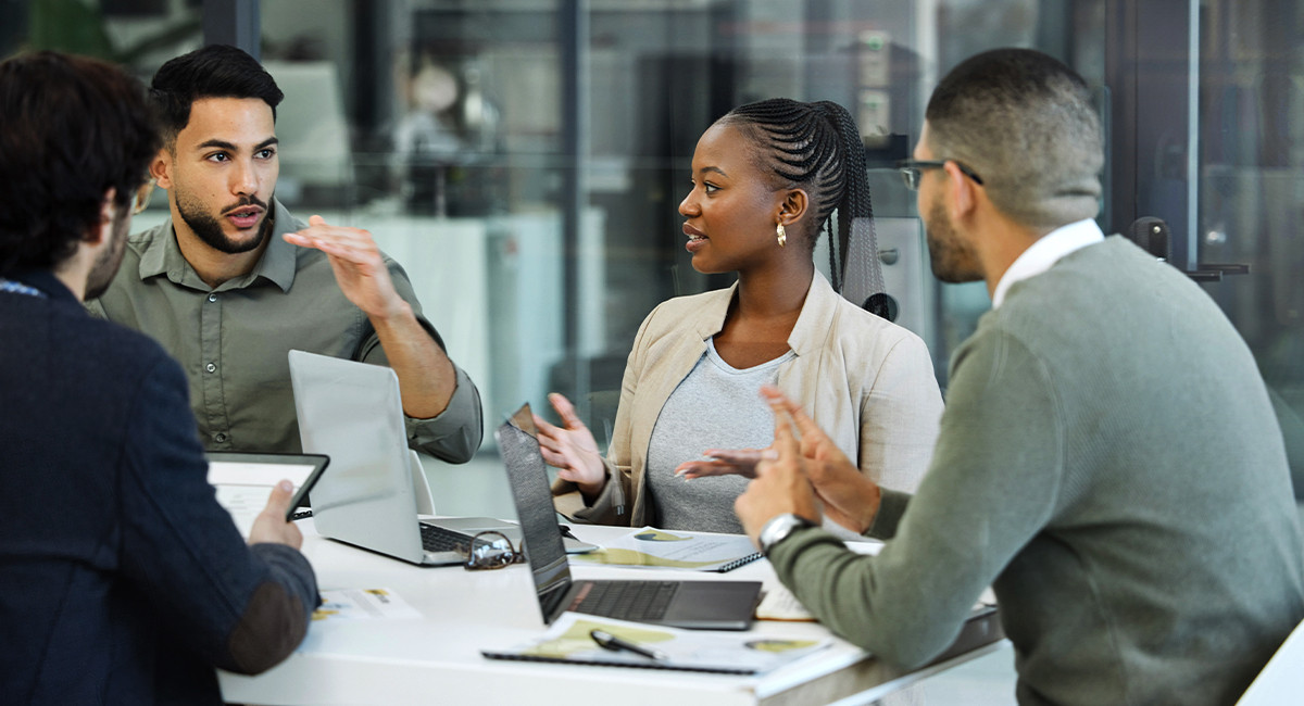 A group of four professionals in an office, intently discussing a complex digital diagram on a large screen.