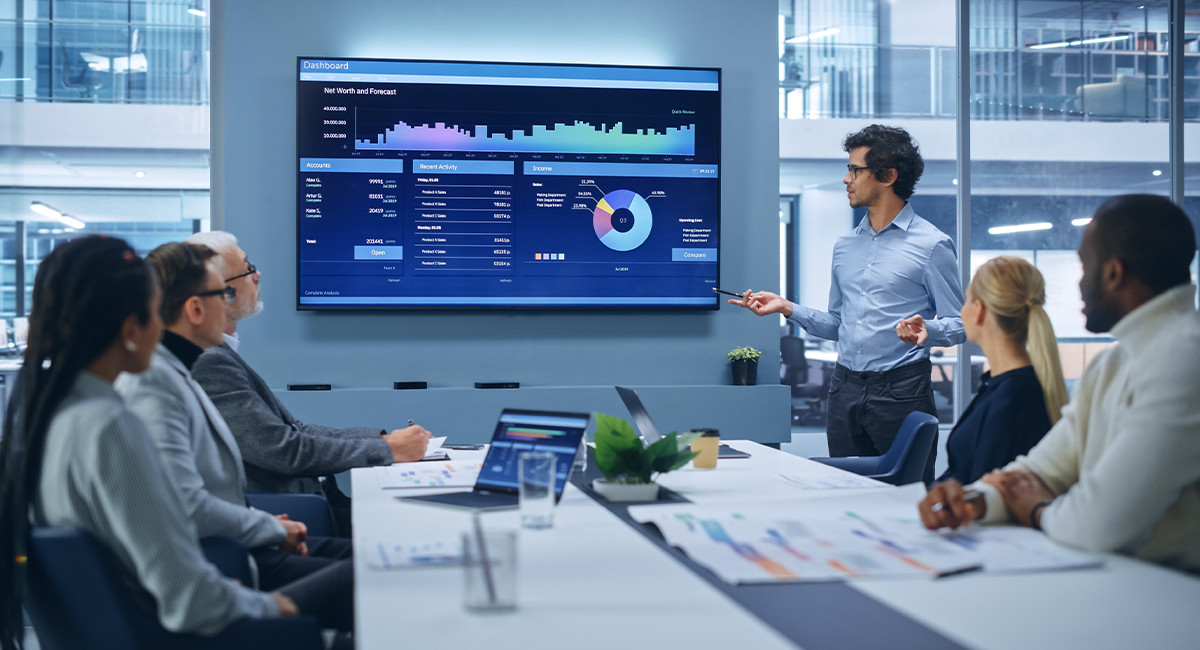 A group of four professionals in an office, intently discussing a complex digital diagram on a large screen.