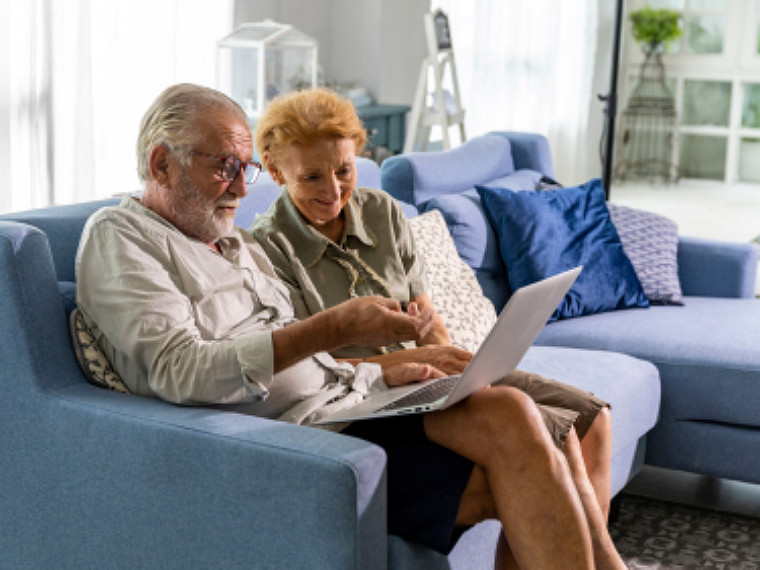 A senior couple sitting on a couch and watching something on a laptop