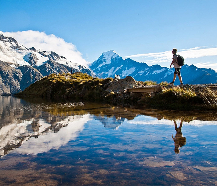 A person hiking near a lake with mountains in the background 