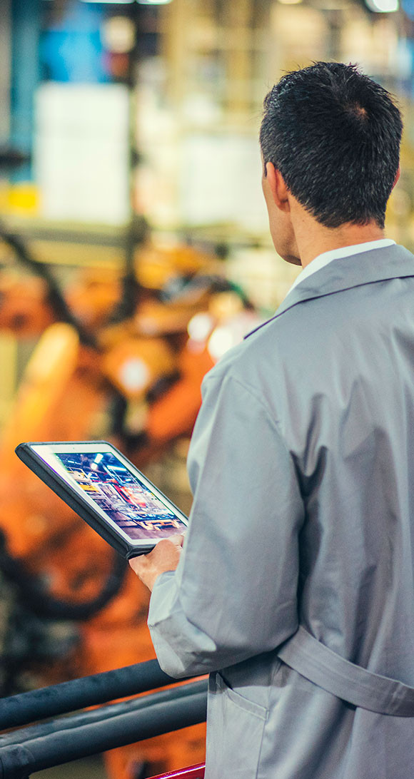 Man in trench coat holding tablet looking out at production site