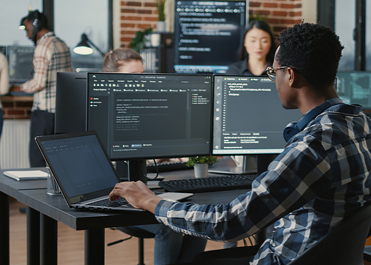 A person looking into multiple desktop monitors and a laptop at work
