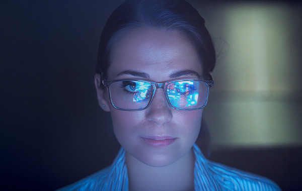 Close-up person wearing glasses reflecting digital screens and data
