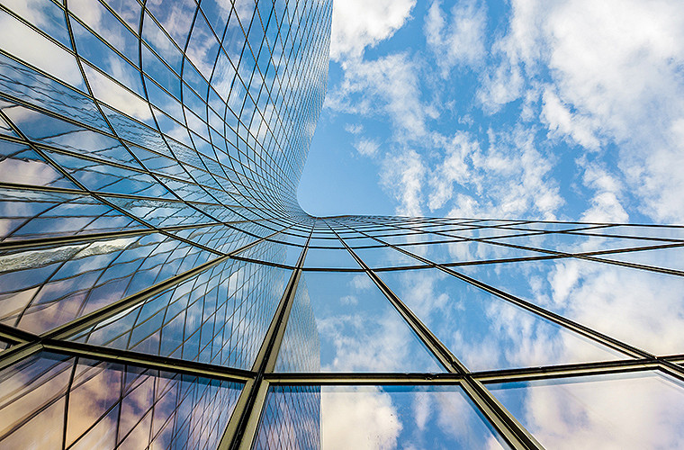 A glass walled building and a blue sky with white cloud captured from a low angle