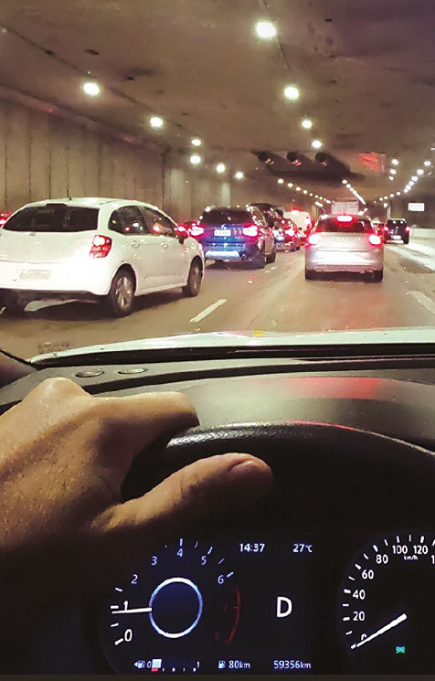 A hand holding a car steering, with multiple other cars in front, in a tunnel.