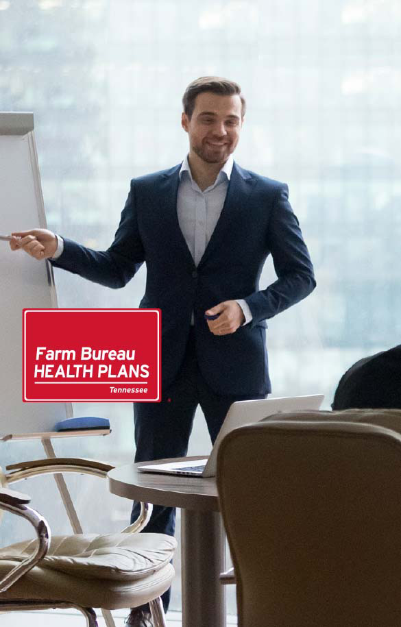 Man in suit standing in front of laptop pointing at whiteboard