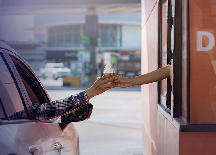 A hand out of a car window at a drive-through taking ice cream from another hand out of a the fast food collection window