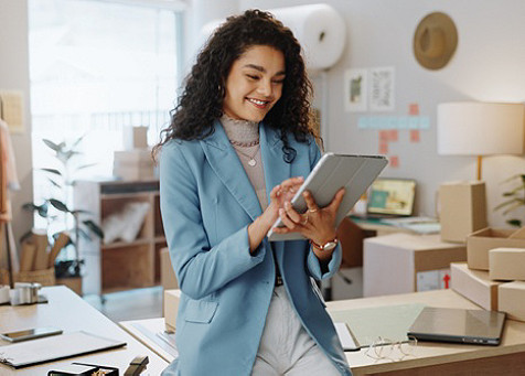 A smiling woman holding a tablet and interacting with it in an office