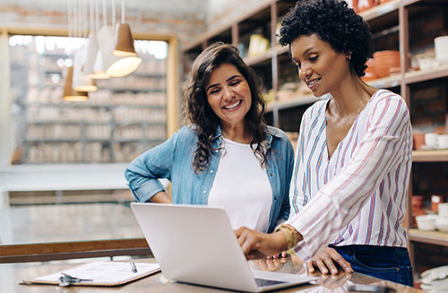 Successful female ceramists using a laptop together in their retail store