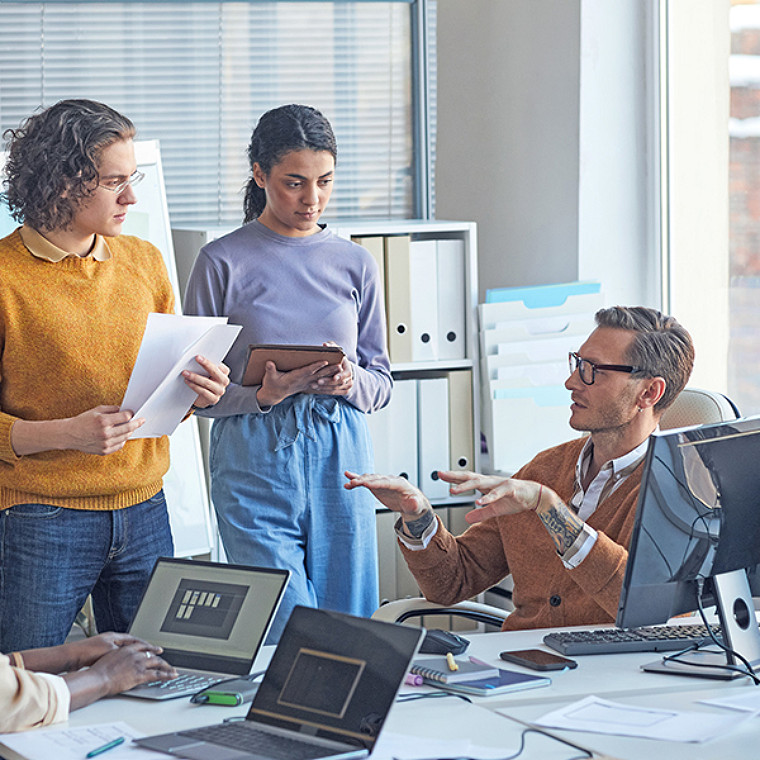 Portrait of diverse software development team collaborating on project in modern office, focus on lead engineer instructing colleagues, copy space