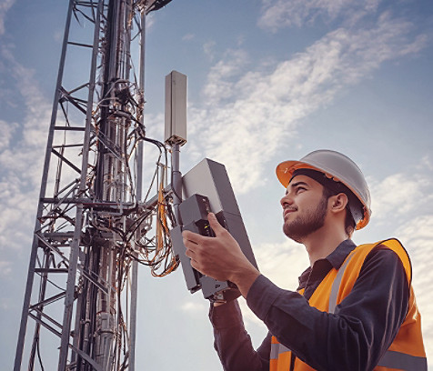 A communications engineer standing next to a telecom tower looking into a digital device